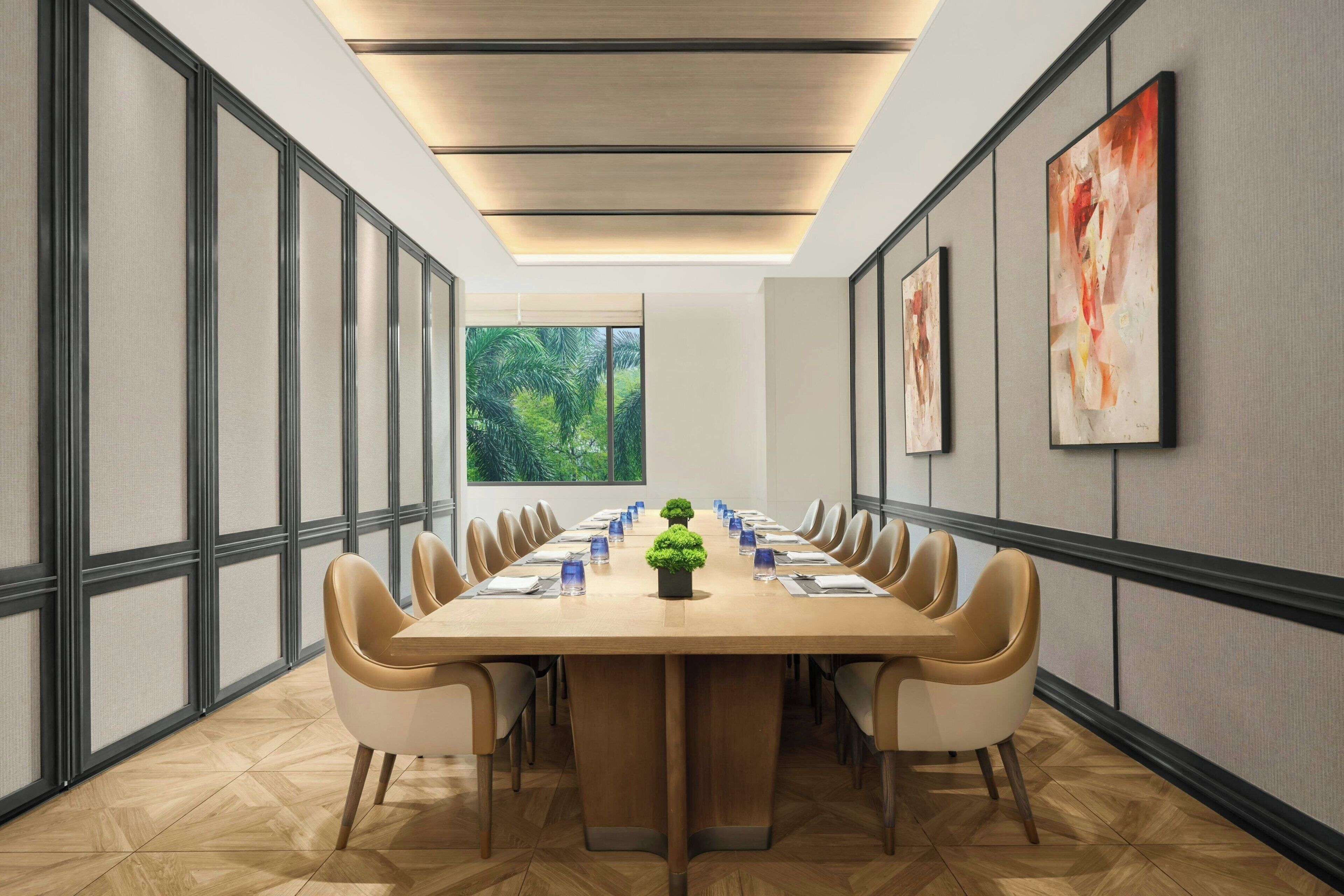 Une salle de conférence avec une longue table, des chaises, une plante en pot et des œuvres d’art encadrées accrochées aux murs.