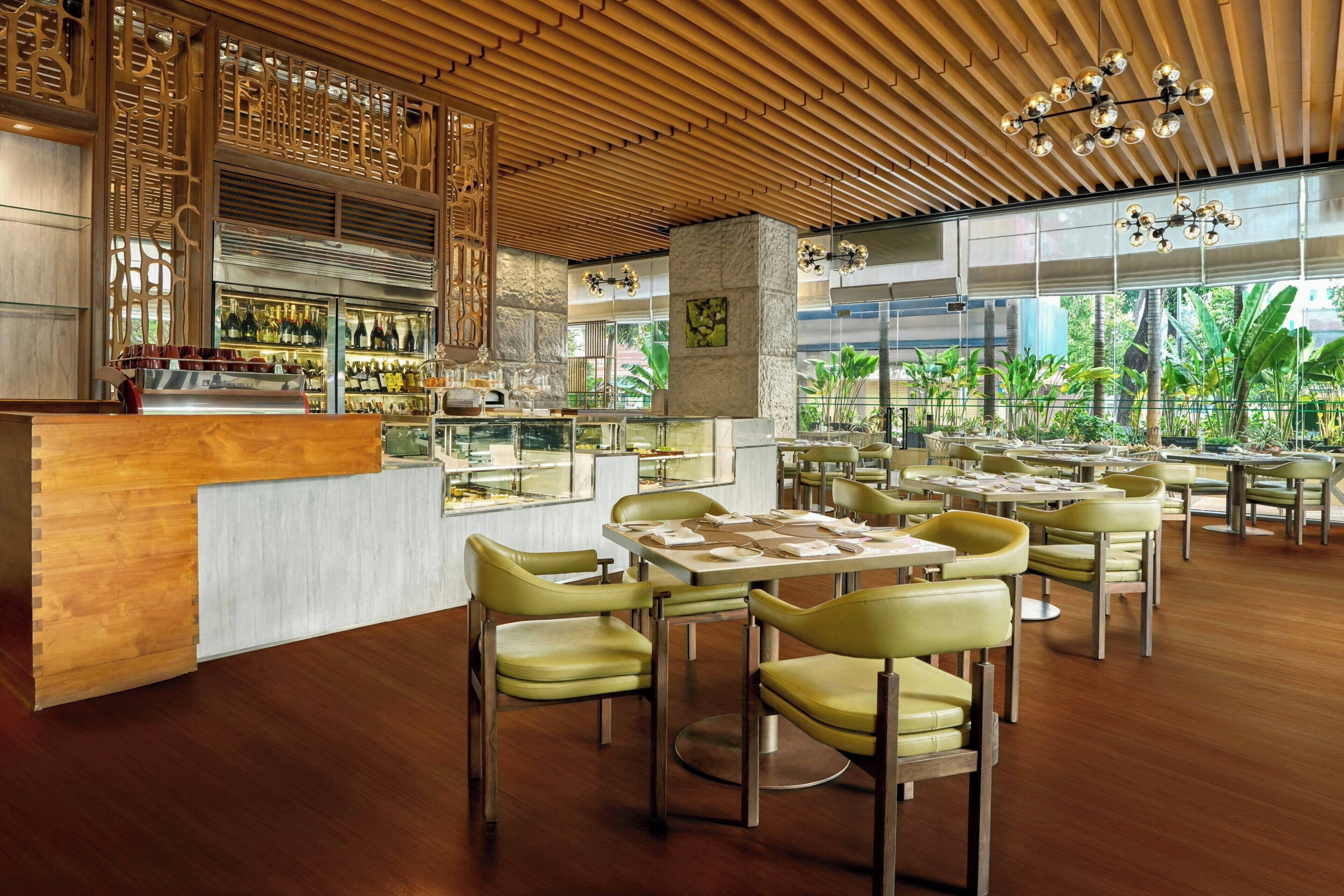 Un restaurante con techo de madera, paredes de vidrio y sillas verdes.
