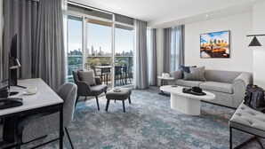 A modern hotel room with a city view, a dining area, a sofa, and a coffee table.