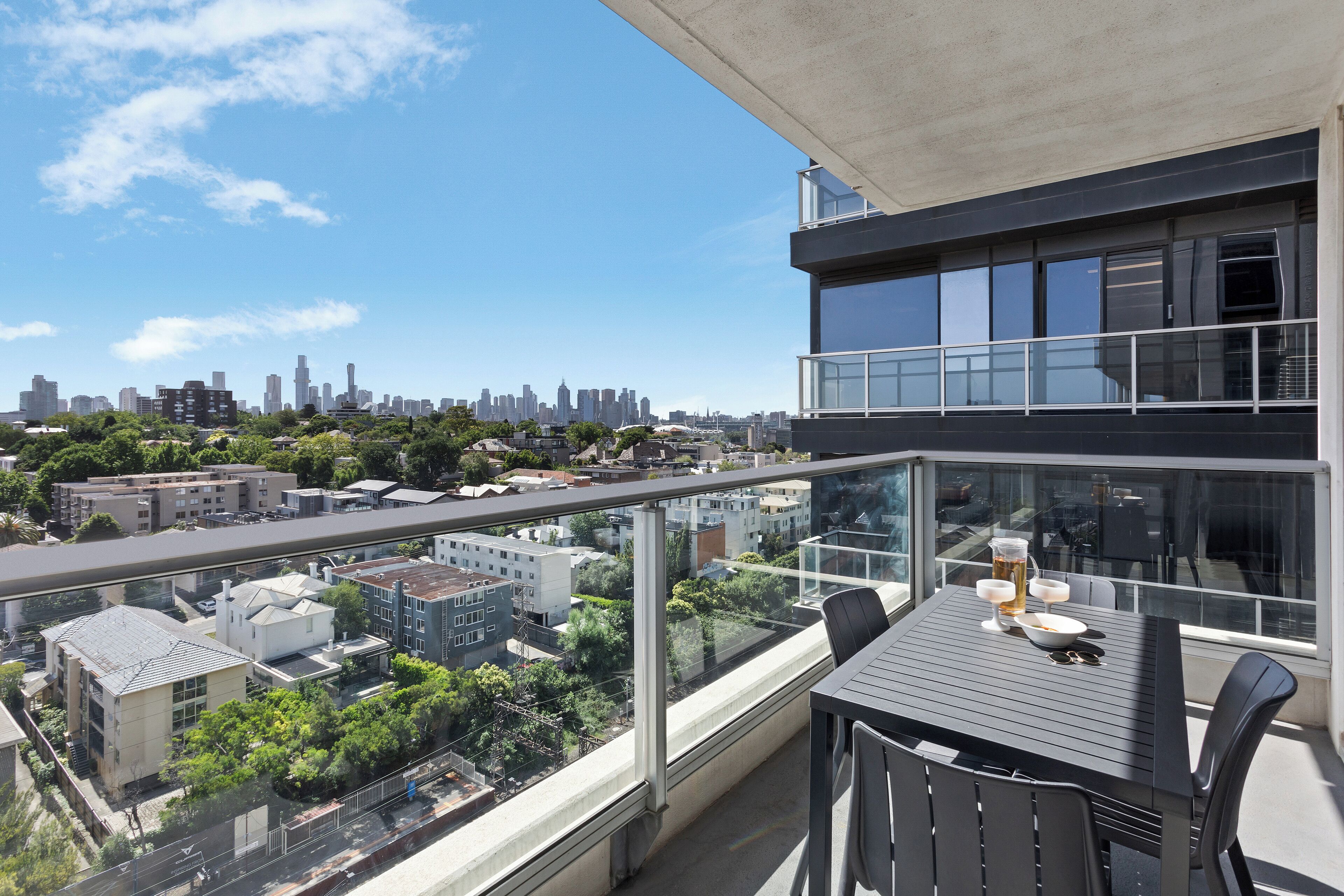 A balcony with a table, chairs, and a city view.