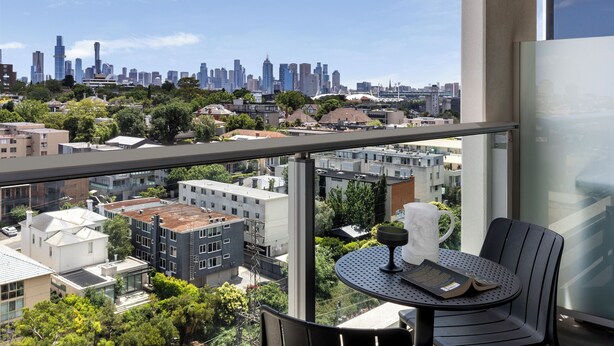 A balcony with a table and chairs, overlooking a cityscape with buildings and trees.