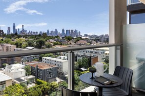 A balcony with a table and chairs, overlooking a cityscape with buildings and trees. - Punthill South Yarra Grand (South Yarra)