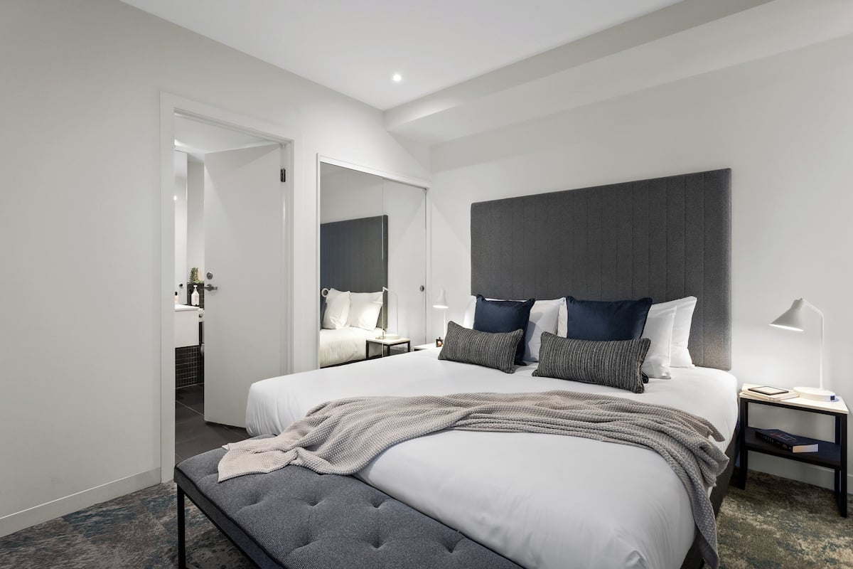Et moderne hotelværelse med en stor seng, et sengebord med lampe og et spejl over sengen.