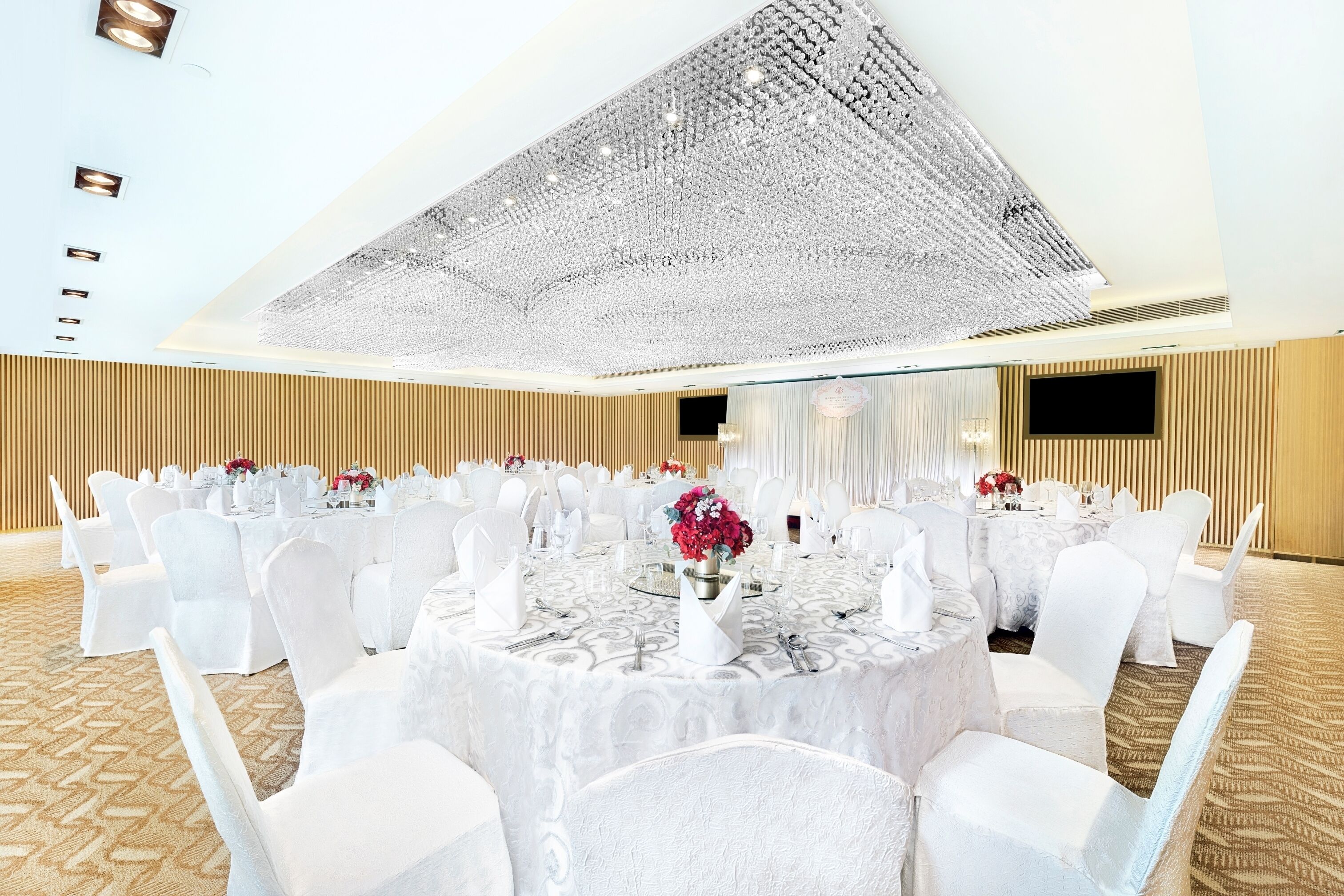 Un salón de banquetes con mesas redondas, sillas blancas y una gran lámpara de araña.