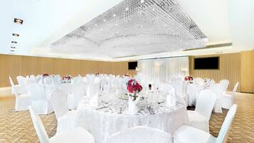 Un salón de banquetes con mesas redondas, sillas blancas y una gran lámpara de araña.