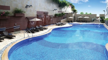 Relax by the pool surrounded by lounge chairs and umbrellas, with a small waterfall feature and steps leading to a covered seating area.