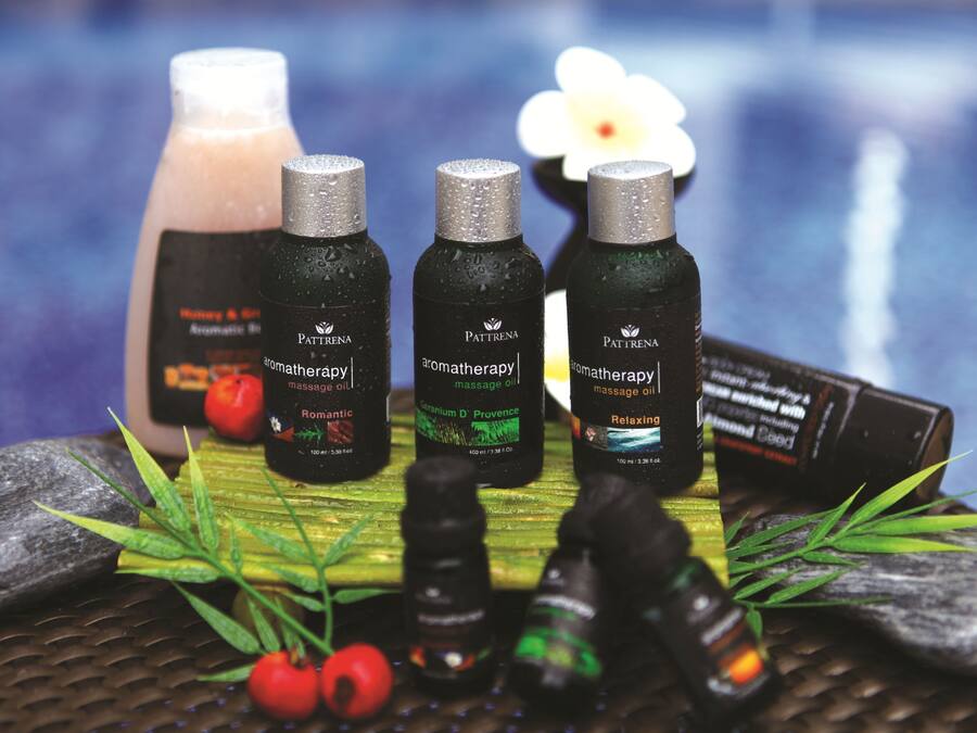 Three bottles of massage oil, a red fruit, and green leaves on a textured surface.