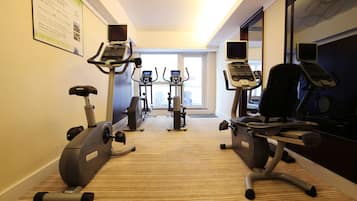 Centro de atividades físicas do hotel, com máquinas de cardio, uma TV na parede e uma janela ampla que oferece iluminação natural.