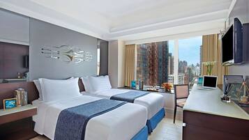 A modern hotel room with two beds, a desk, a TV, and a city view.