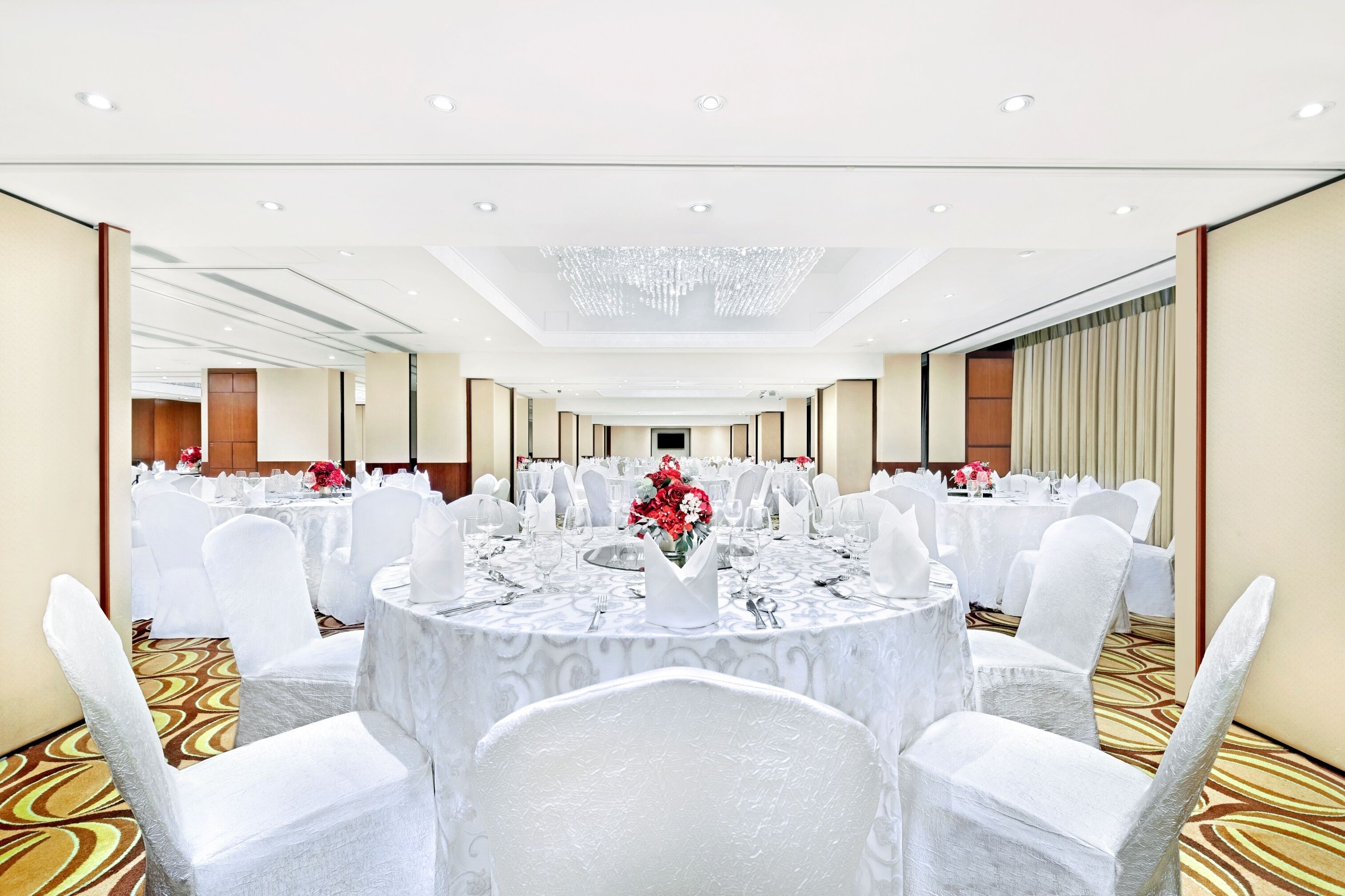 A banquet hall with round tables, white chairs, and a chandelier.