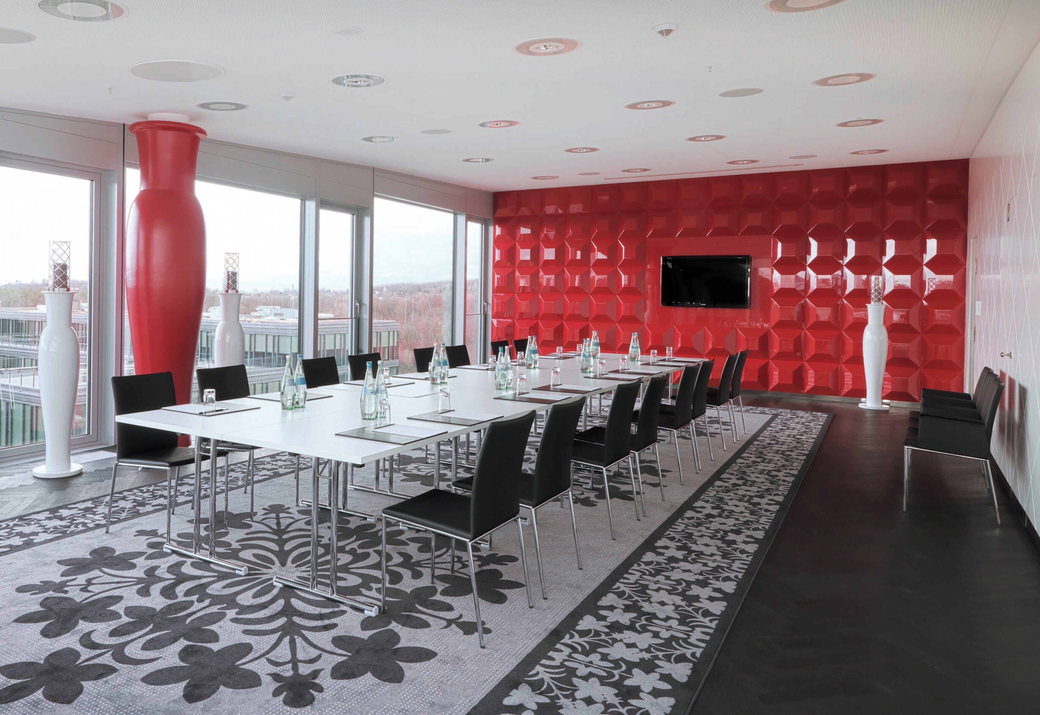 Ein Konferenzraum mit einem langen Tisch, schwarzen Stühlen und einem gemusterten Teppich.