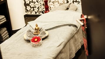 A massage table with a towel, a small Buddha statue, and a flower in a glass container.