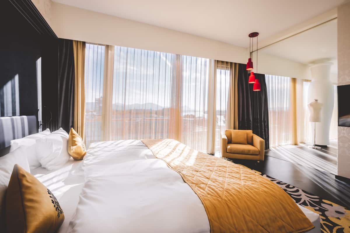 A hotel room with a large bed, a chair, a TV, and a view of the city.