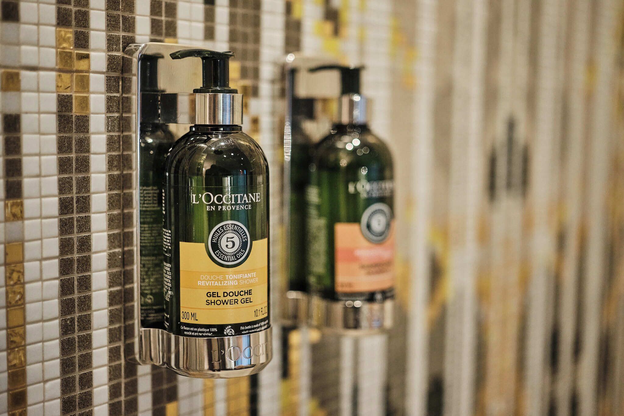 A shower area with L'OCCITANE shower gel dispensers mounted on a tiled wall.