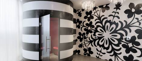A modern bathroom with a curved glass partition, a shower area, and a decorative wall with a floral pattern.