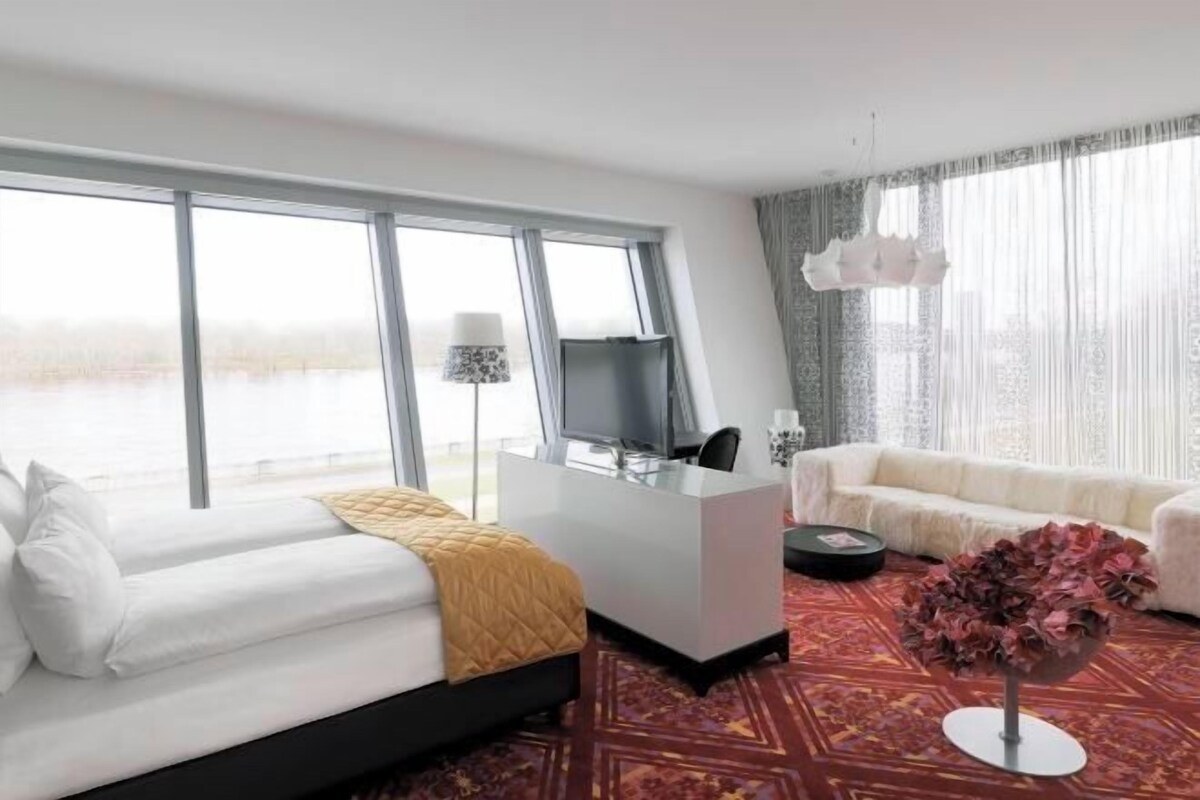 A hotel room with a bed, a desk, a chair, a sofa, and a decorative plant.