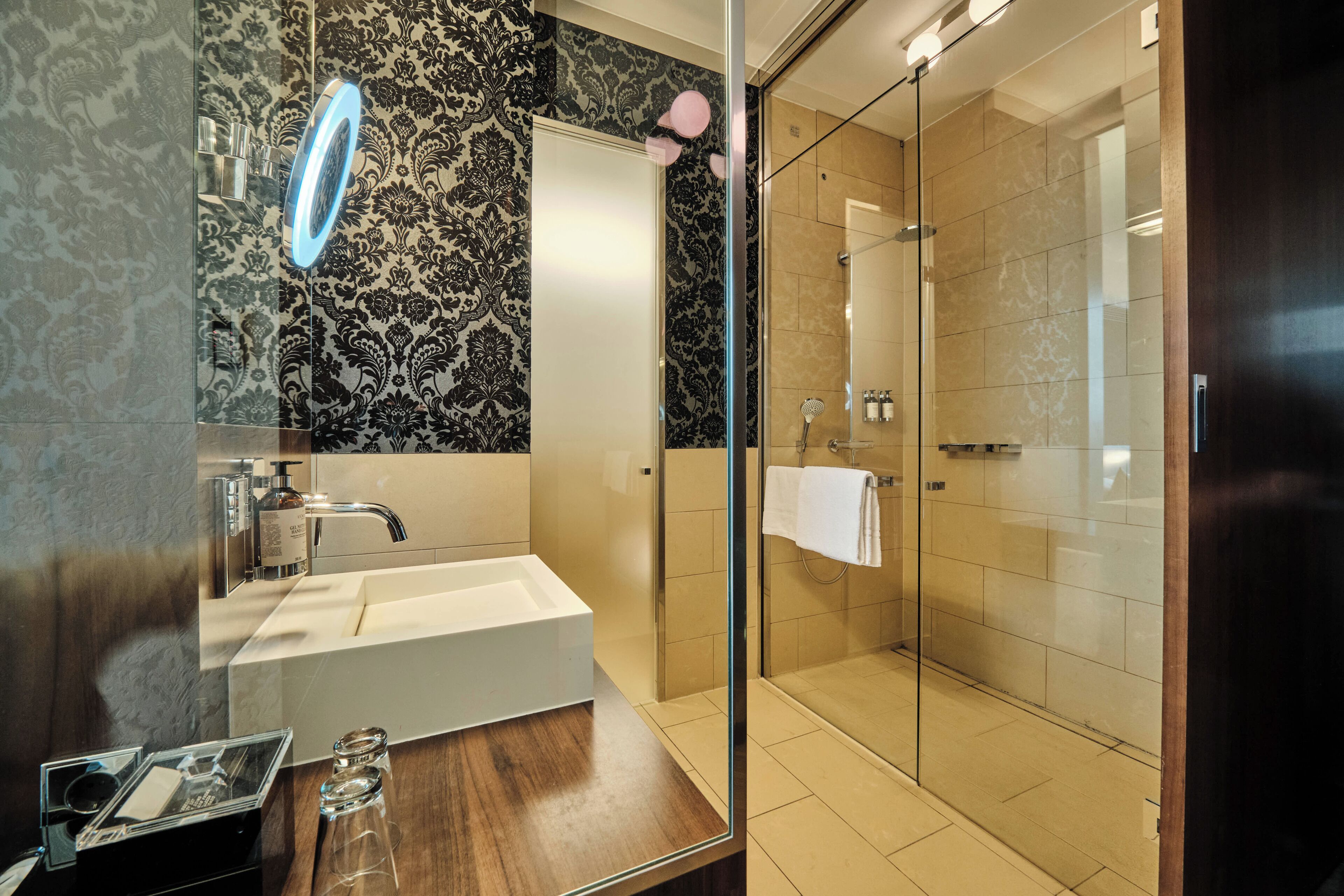 A modern bathroom with a glass-enclosed shower, a large mirror, and a white sink.