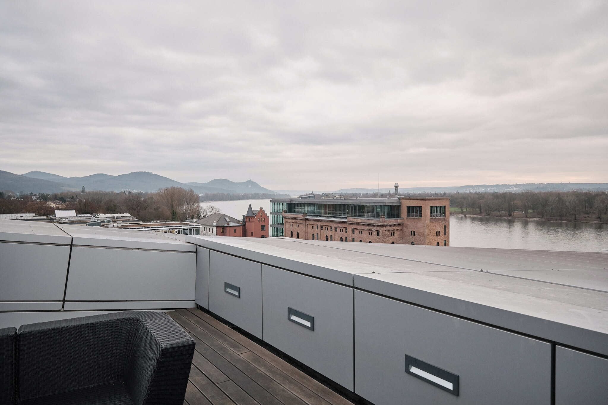 Una terraza en la azotea con vistas a un río, montañas y edificios.