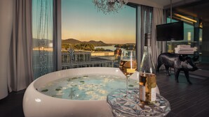 Une chambre dotée d’une grande fenêtre, d’un jacuzzi, d’une bouteille de vin et d’un téléviseur.
