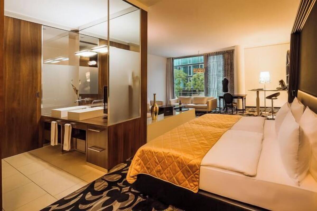 A hotel room with a bed, a large mirror, a desk, a chair, and a view of the outdoors.
