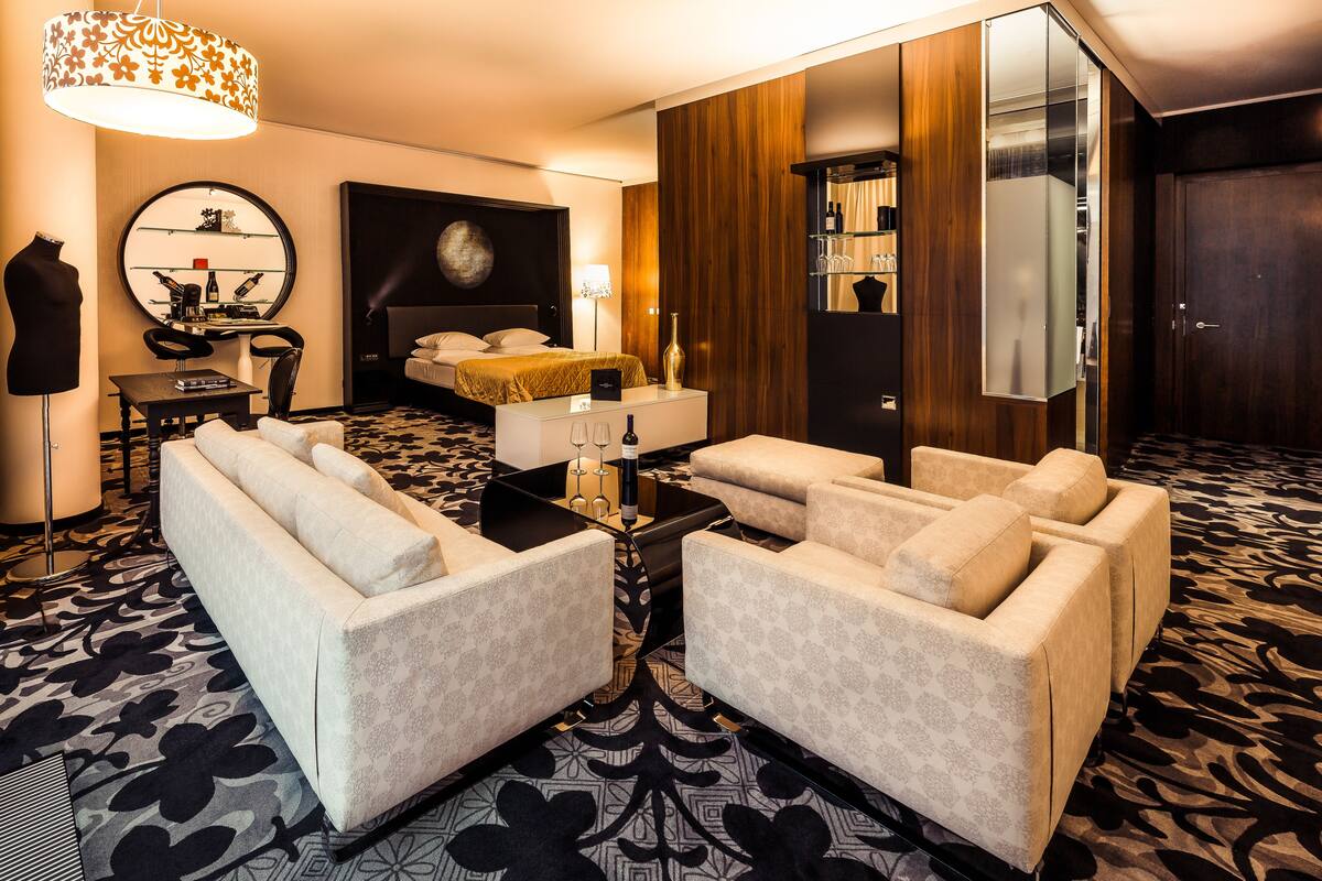 A modern hotel room with a large bed, two sofas, a desk, and a mirror.