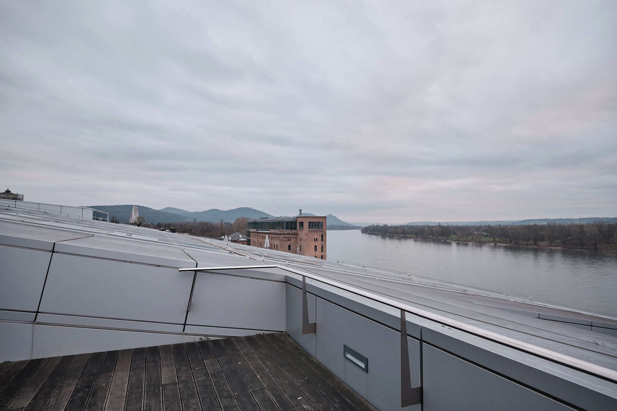 A view from a balcony overlooking a river, with a modern building and mountains in the background.