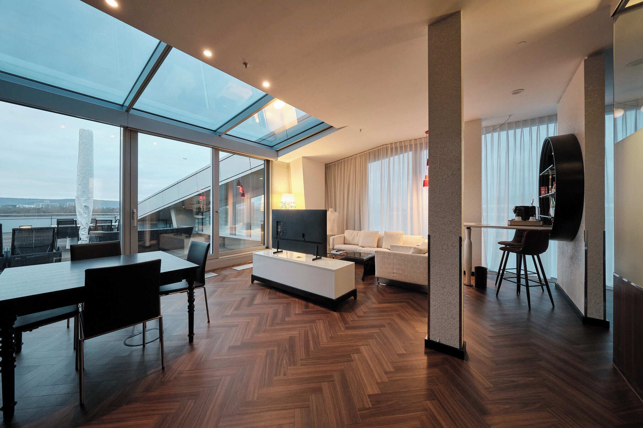 Un salon moderne doté d’une grande baie vitrée, d’un téléviseur à écran plat, d’un canapé et d’un coin repas avec une table et des chaises.