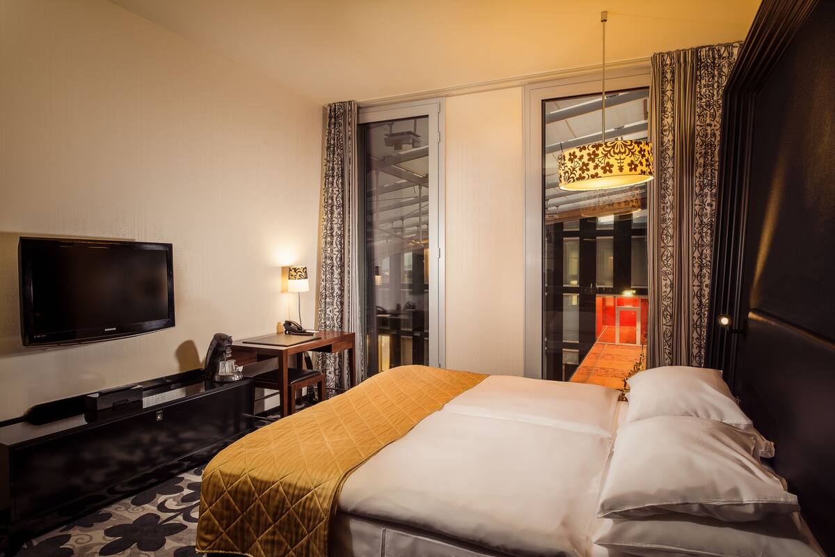 A hotel room with a bed, a desk, a television, and a window with curtains.
