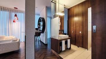 Una habitación de hotel moderna con sofá, comedor, espejo grande y armario de madera.