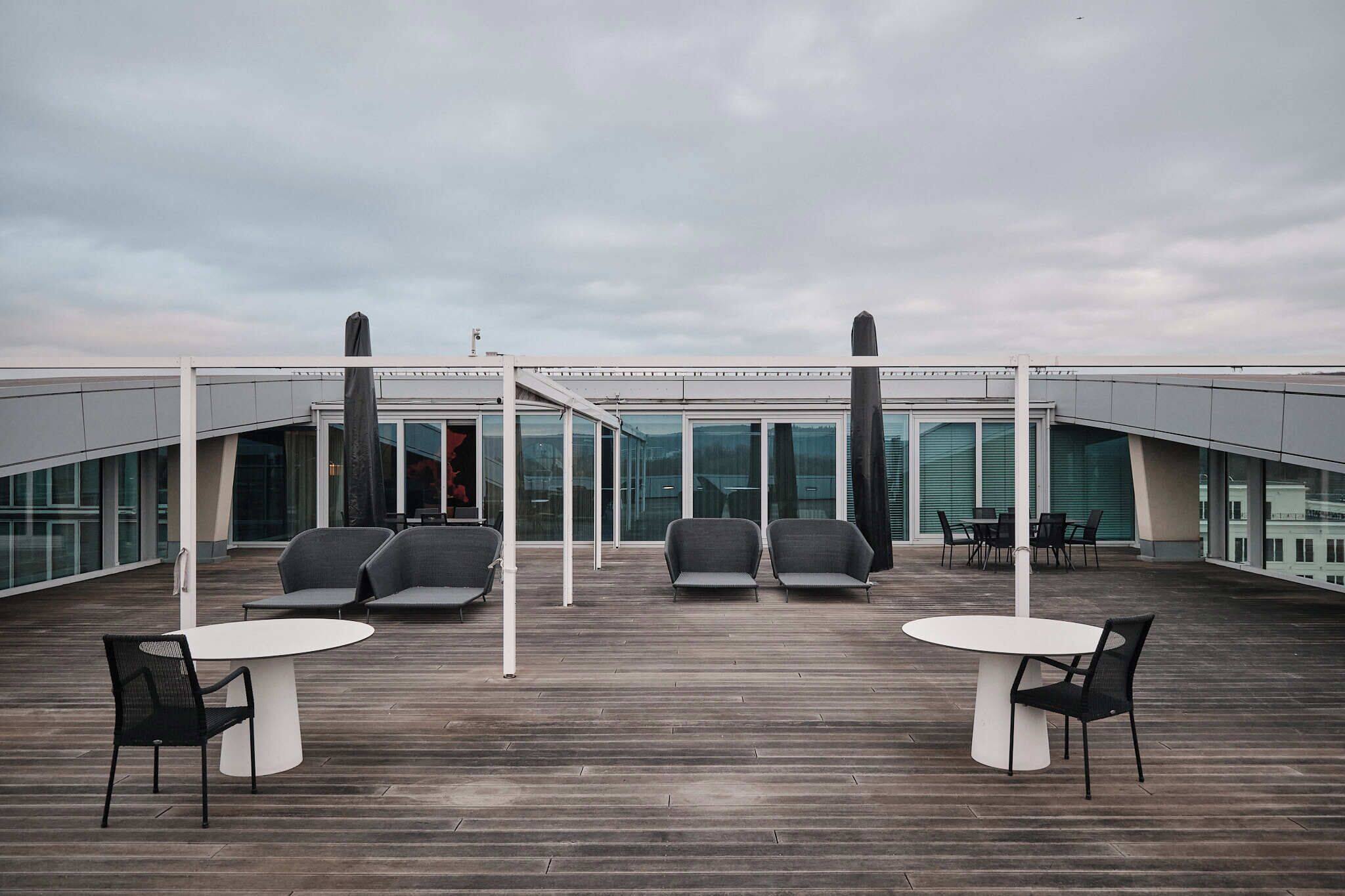A rooftop terrace with seating arrangements and a glass-enclosed building in the background.