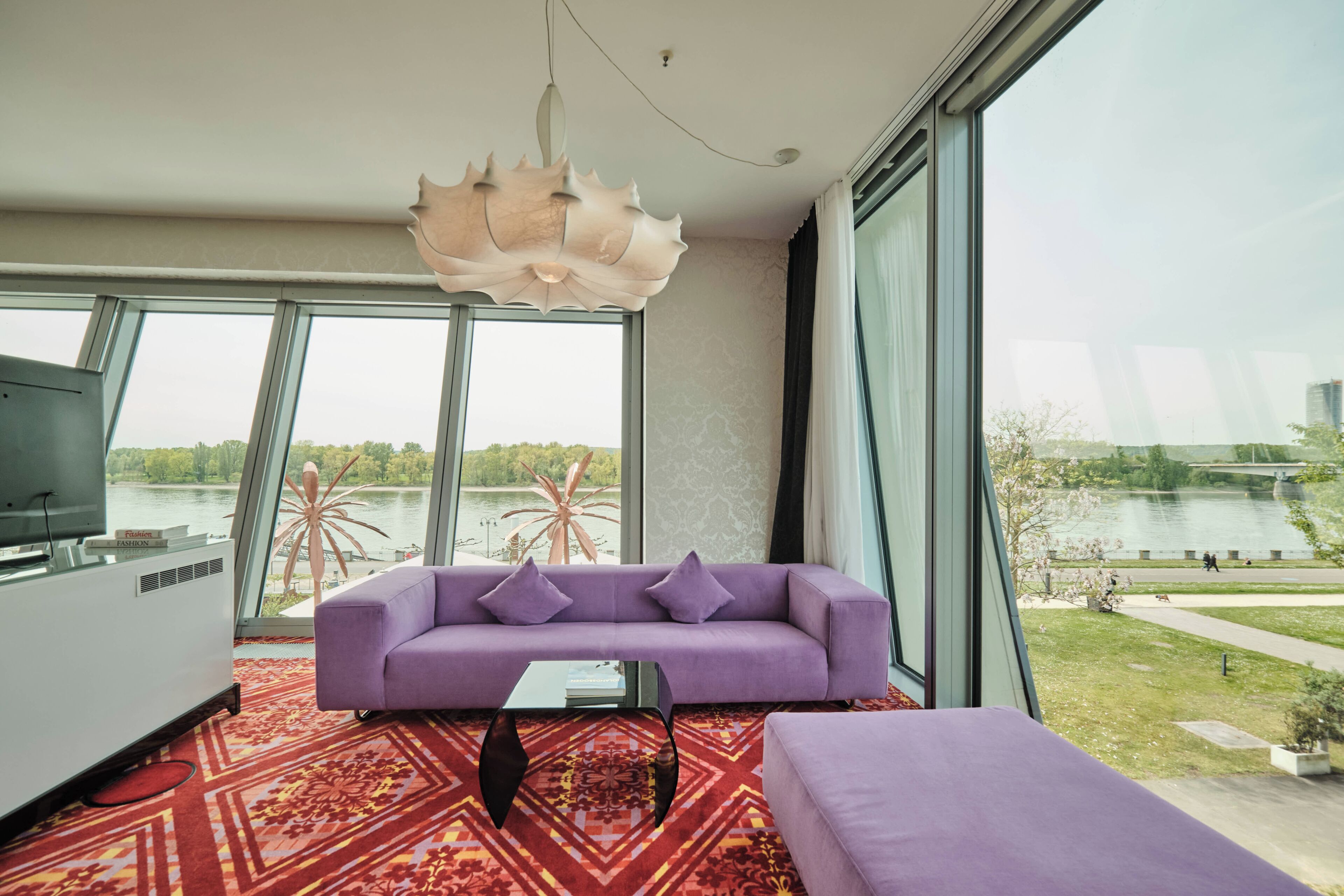 A modern living room with a purple sofa, a large window, and a view of a lake.