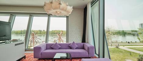 A modern living room with a purple sofa, a large window, and a view of a lake.
