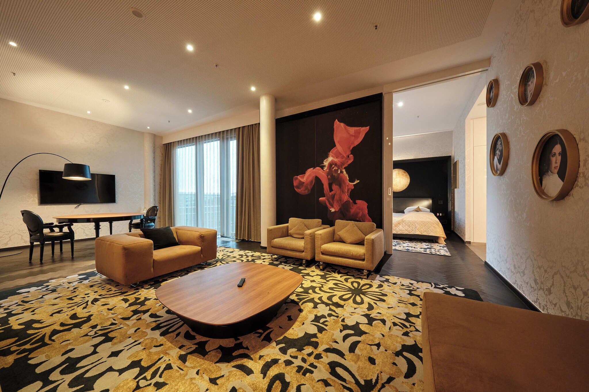 A modern hotel room with a large bed, two sofas, a coffee table, a TV, and a large window.