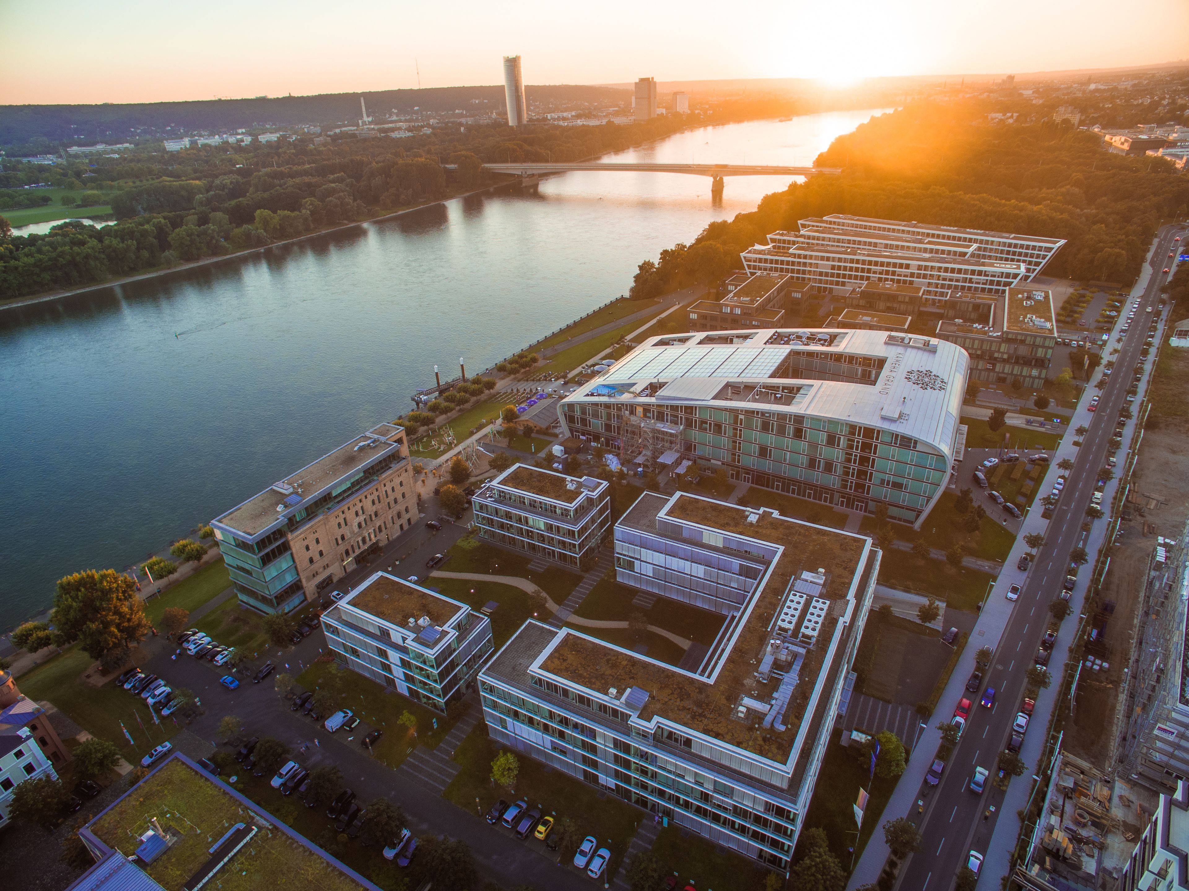 An aerial view of a modern building complex with multiple structures, a parking lot, and a river in the background.