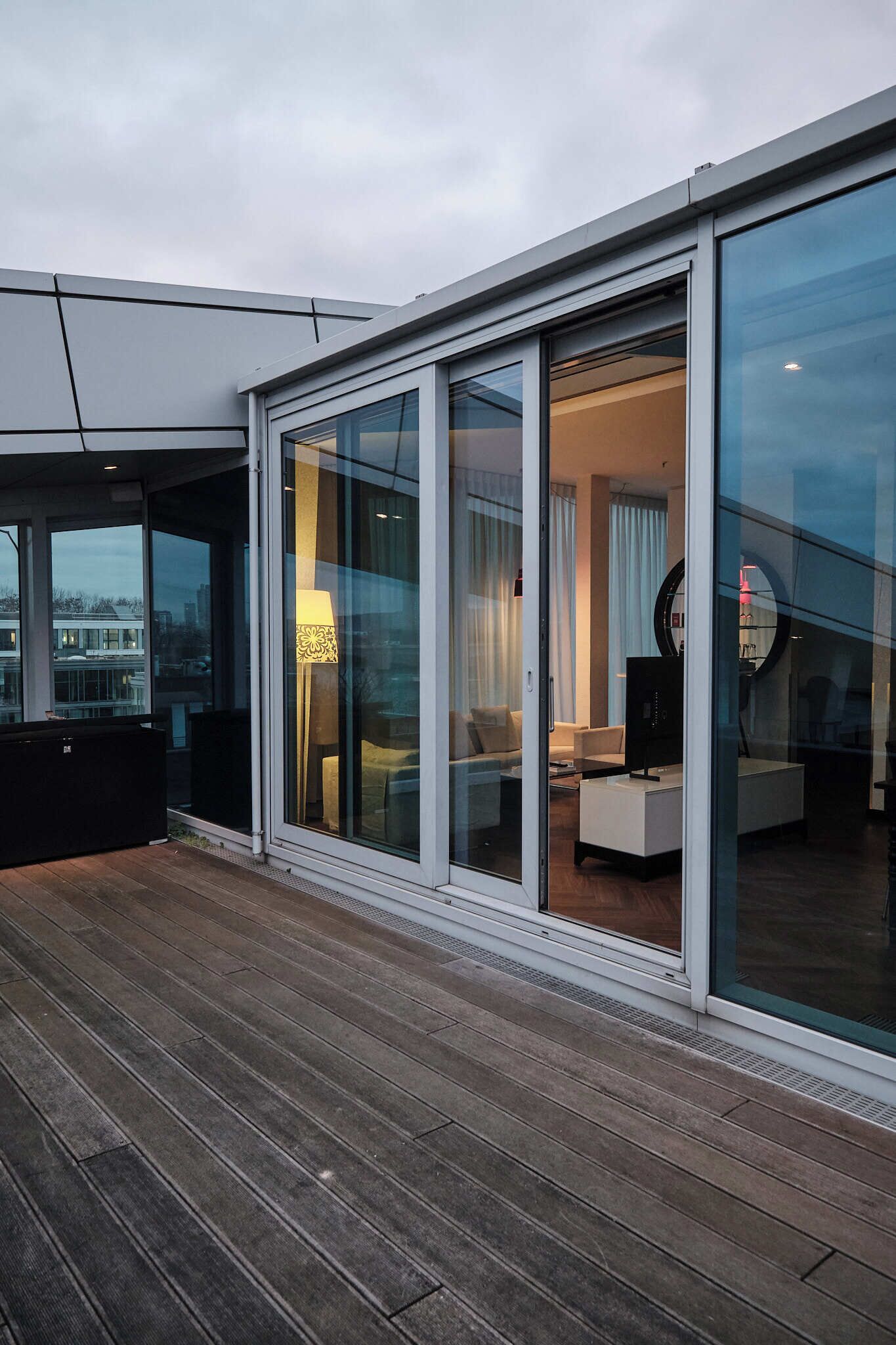 A modern hotel room with large sliding glass doors, a wooden deck, and a view of the cityscape.
