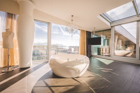 Una sala de estar moderna con un ventanal grande, una bañera blanca y un candelabro.