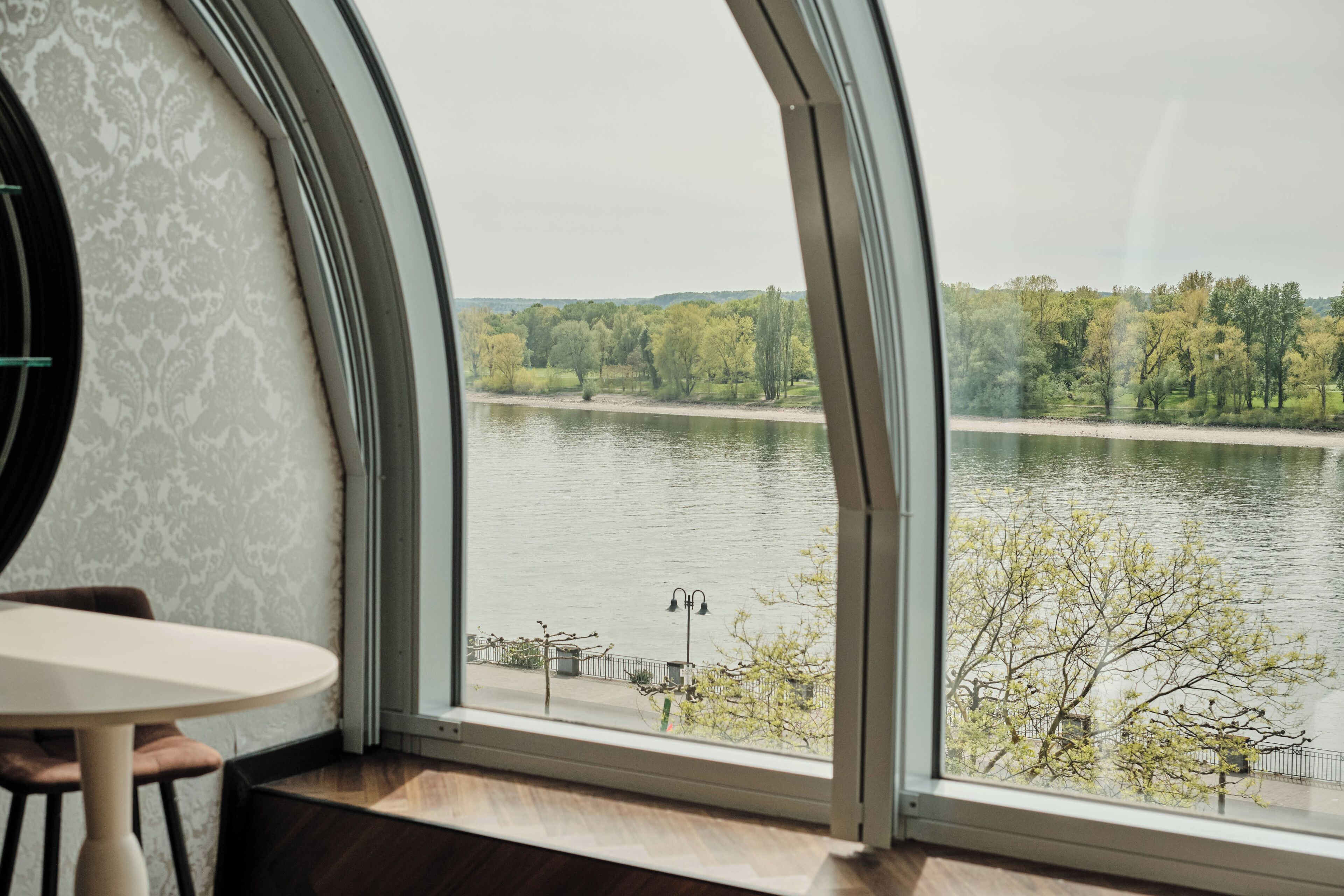 A room with a curved window overlooking a river and trees.