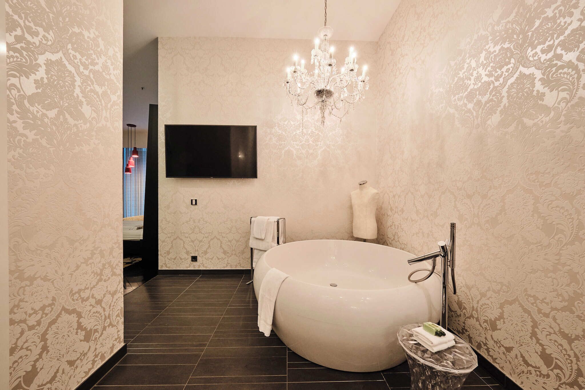 A modern bathroom with a large bathtub, a chandelier, and a flat-screen TV mounted on the wall.