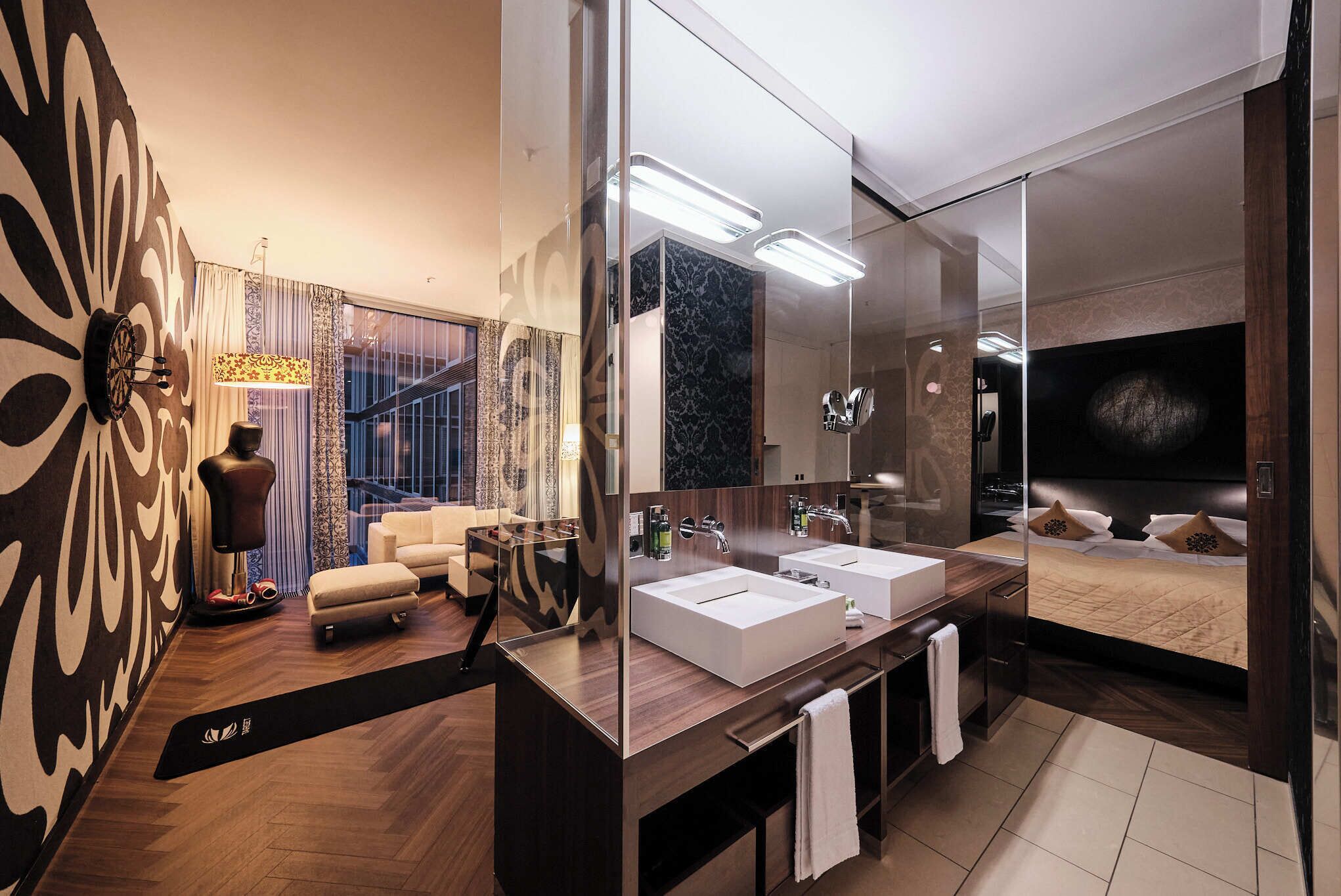 A modern bathroom with two sinks, a large mirror, and a bed with a TV.