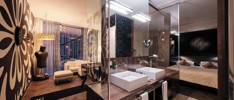 A modern bathroom with two sinks, a large mirror, and a bed with a TV.