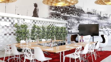 Una sala de conferencias moderna con una gran mesa, sillas blancas, alfombra roja y una pantalla grande.