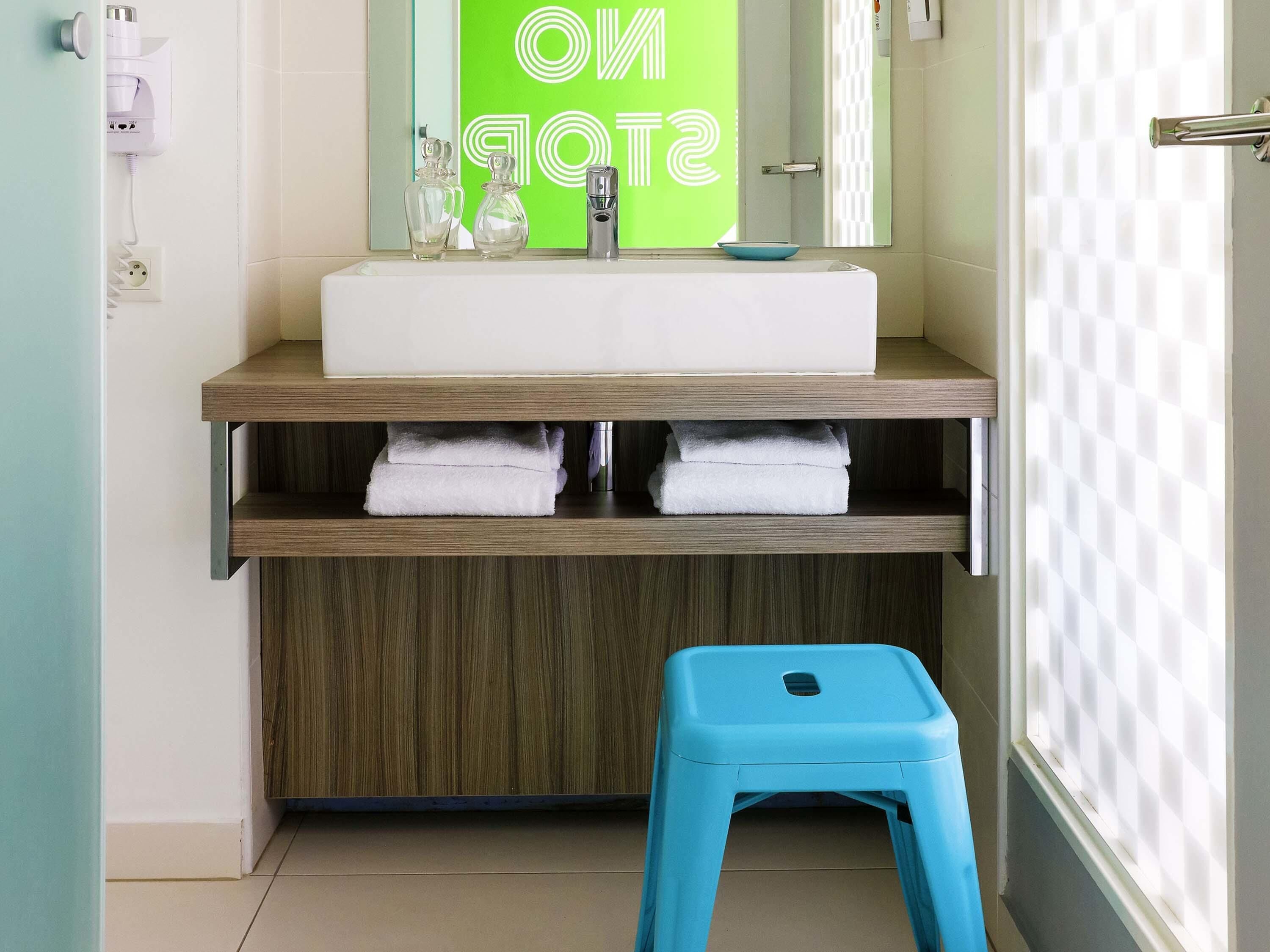 A bathroom with a white sink, a mirror, and a blue stool.
