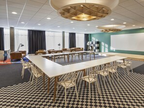 Un salón de conferencias con una gran mesa, sillas, una pantalla de proyector y un suelo estampado.