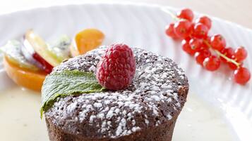 Un postre con pastel de chocolate, frambuesas y diversas frutas sobre un plato.
