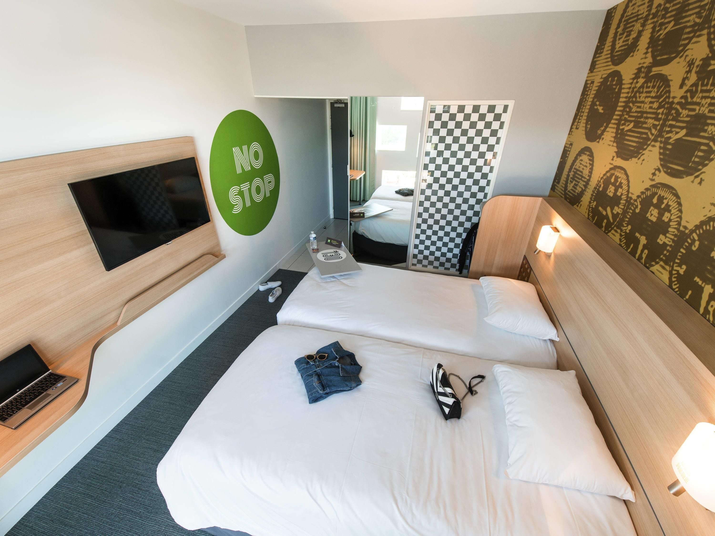 A hotel room with two beds, a TV, a laptop, and a 'NO STOP' sign on the wall.