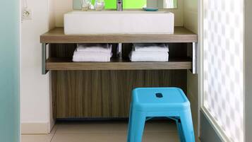 A bathroom with a white sink, two glass bottles, a blue stool, and a green mirror.