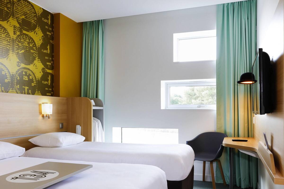 Hotelkamer met twee bedden, een bureau, een stoel, een televisie en een raam met gordijnen.