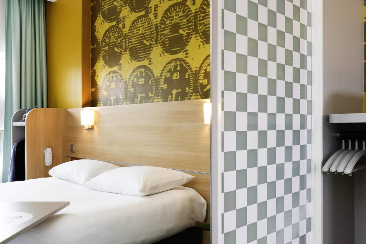 Une chambre d’hôtel avec un lit, une tête de lit, un mur à motifs à carreaux et un mur décoré d’un motif représentant une horloge.