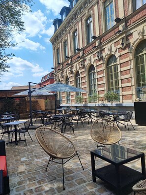 An outdoor café with tables and chairs, a brick building in the background, and a clear sky.
