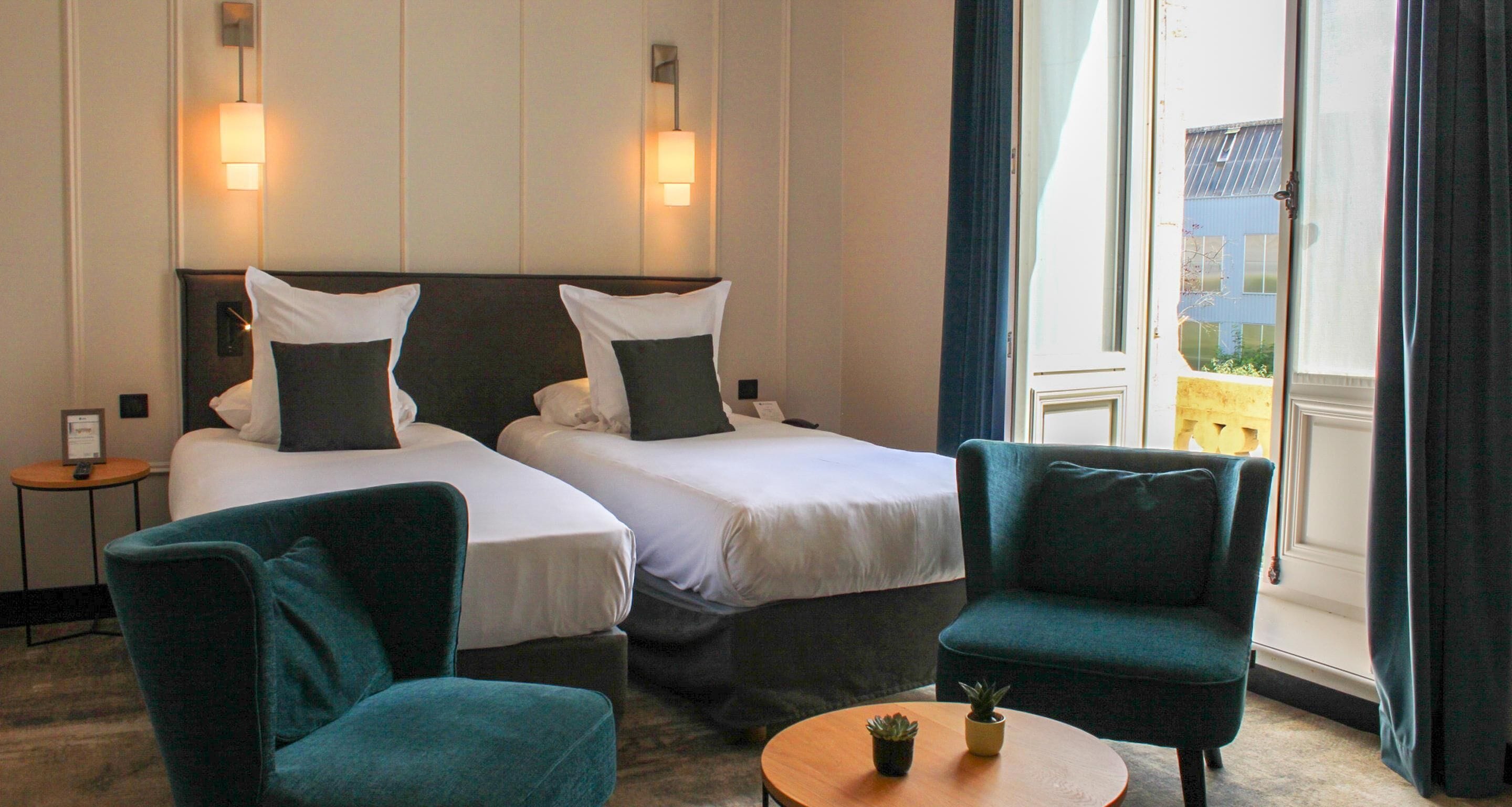 A hotel room with two beds, a small table with a plant, and a view of the outside through a large window.
